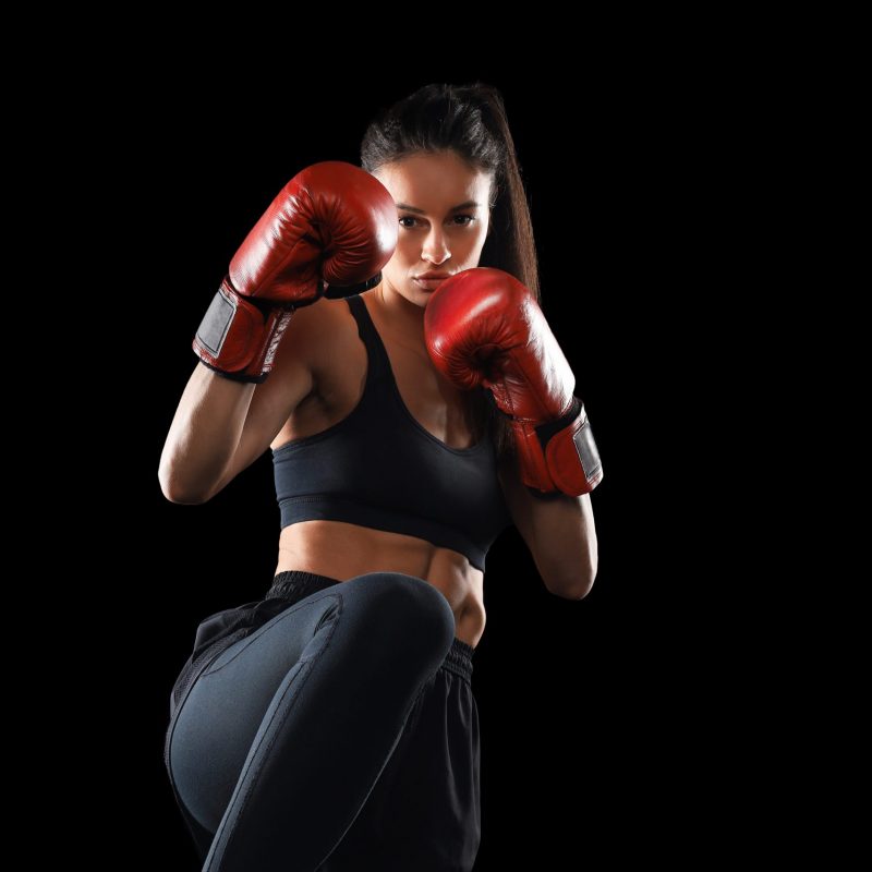 Kickboxing woman in activewear and red kickboxing gloves on black background performing a martial arts kick. Sport exercise, fitness workout