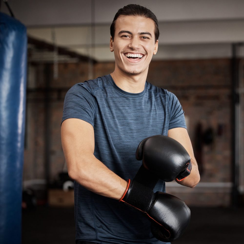 Fitness, portrait and man with boxing gloves in gym for training, exercise or training. Happy, smile and male athlete or boxer doing cardio kickboxing workout for health or wellness in sports studio